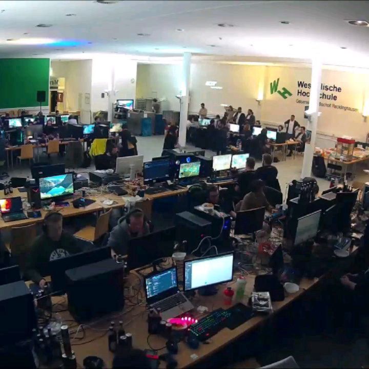Blick von oben auf dicht belegte Computertische in der abgedunkelten Mensa mit leuchtenden Bildschirmen.