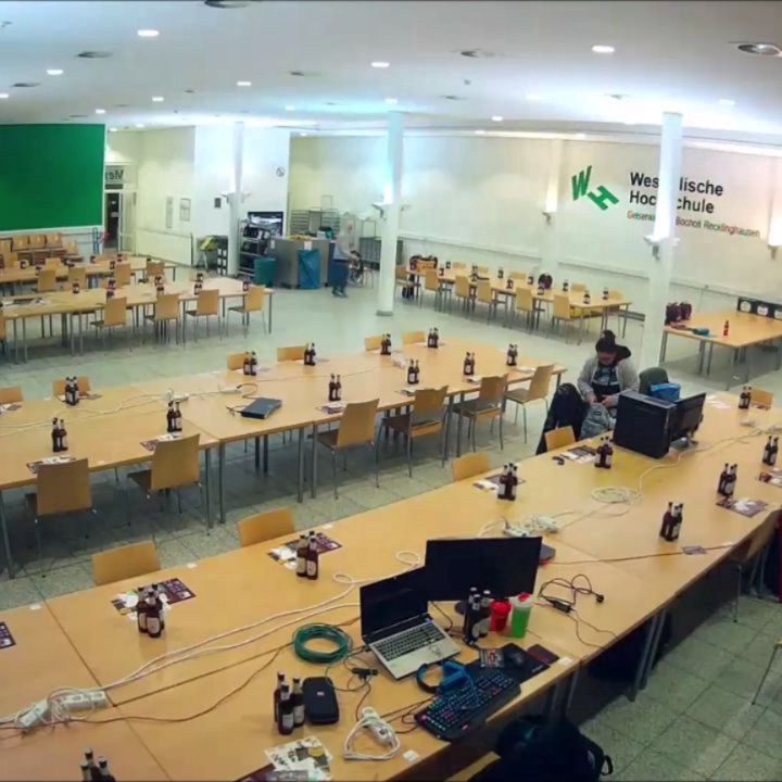 Blick über die noch weitgehend leere Mensa: Auf langen Tischreihen stehen einzelne Monitore und Computer bereit.