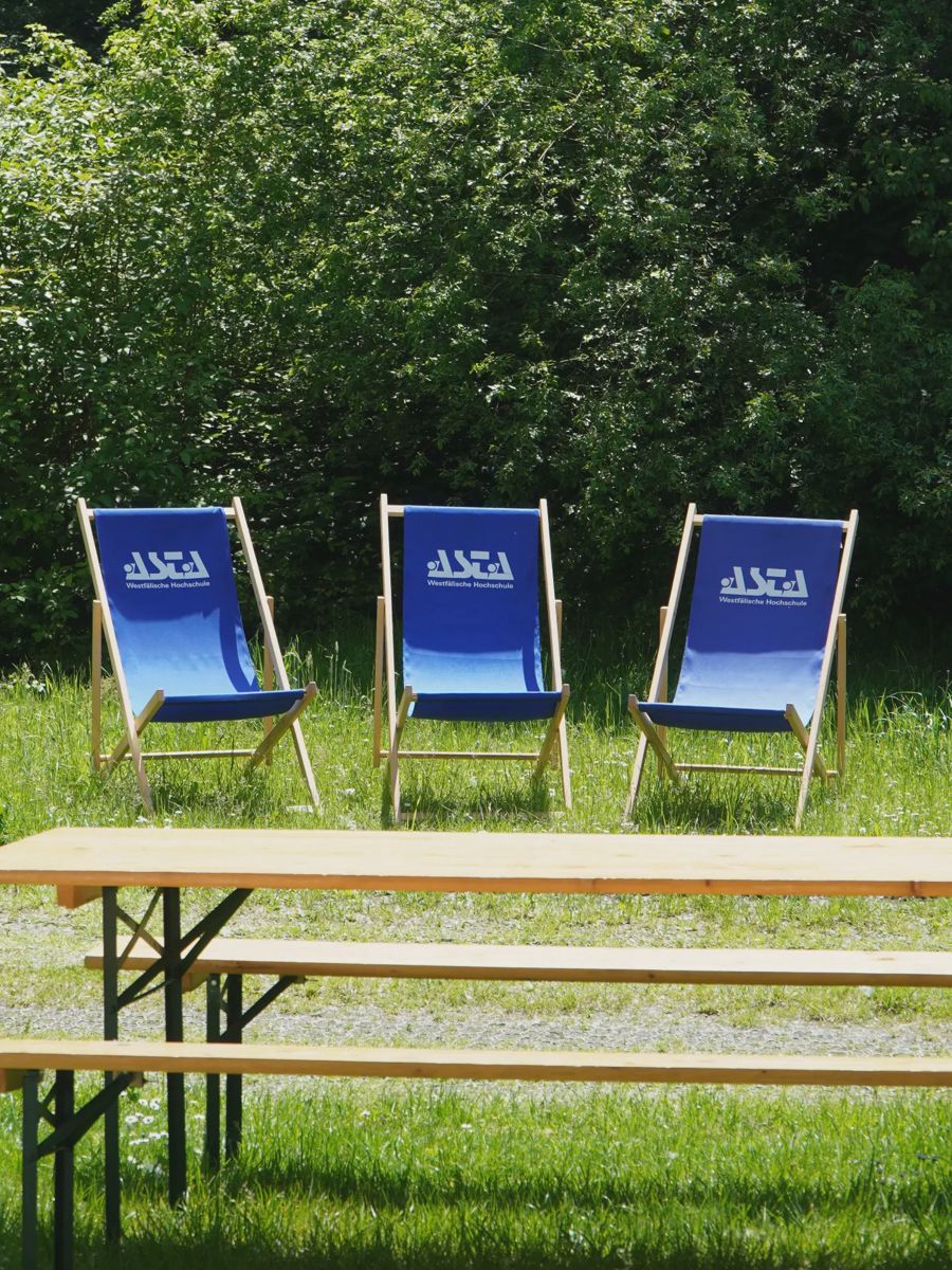 Drei blaue Liegestühle stehen hinter einer Bierzeltgarnitur auf der Wiese.